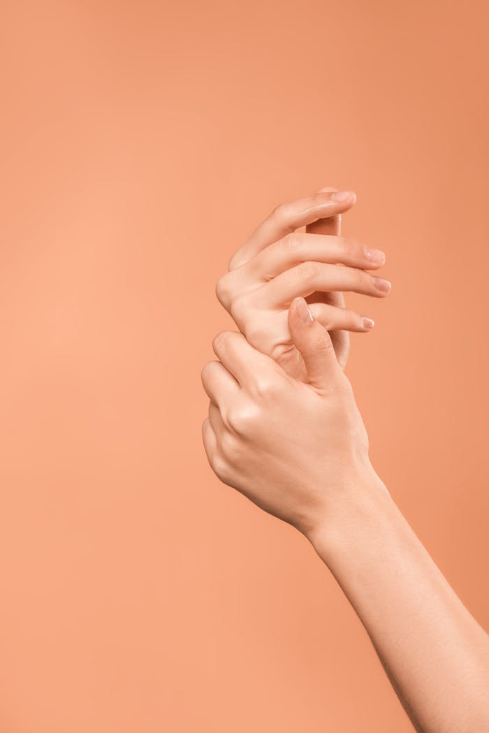 Close-up of soft, smooth hands with elegant pose on a peach background, showcasing skincare beauty.